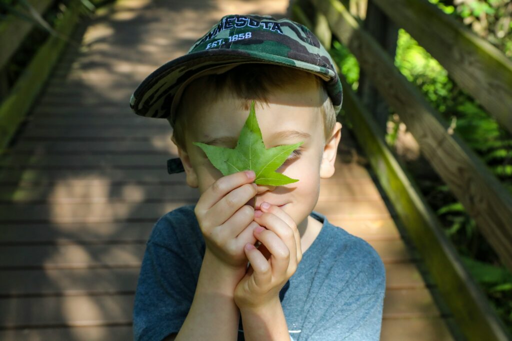 Outdoor Forest School student holding a sweetgum leaf playfully in front of face